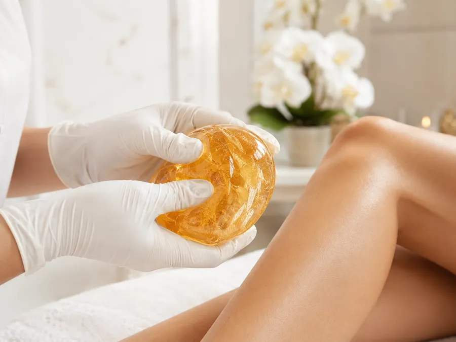 Sugaring: goldene Zuckerpaste in behandschuhten Händen vor der Anwendung